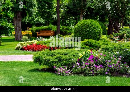 Blumenbeet mit Pflanzen in einem Freizeitpark mit Wegen und Holzbänken im Schatten unter den Bäumen. Stockfoto