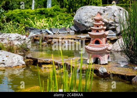 Künstlicher Teich mit Wasserfall und einer Skulptur eines japanischen Hauses im Wasser. Stockfoto