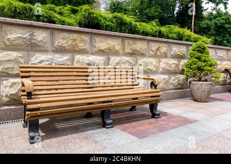 Eine Bank aus Holzbrettern und eisernen Beinen im Hinterhof mit Steinblumentöpfen und Wänden mit einem rustikalen und immergrünen Arborvitae. Stockfoto