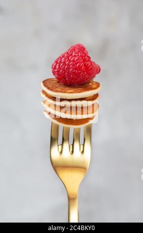 Winzige Cerealien-Pfannkuchen mit Himbeeren auf einer Gabel auf dunklem Hintergrund aufgereiht Stockfoto