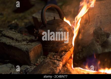 Der Wasserkocher wird nachts an einem hellen Feuer im Freien erhitzt Stockfoto
