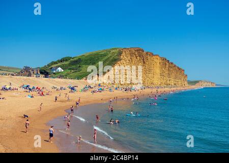 West Bay Beach Dorset, Großbritannien. Am Meer mit Menschen genießen das Sommerwetter am Strand und paddeln im Meer. Stockfoto
