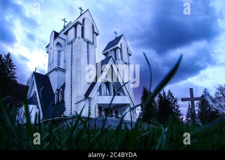 Gruseliger Friedhof mit Kirche im Hintergrund. Ein Kreuz ist gegen den dunklen Himmel zu sehen. Stockfoto