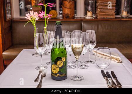 Eine Flasche Franciacorta Gualberto vom Gut Ricci Curbastro steht neben einem Glas Schaumwein auf einem gedeckten Tisch im Hotel und Restaurant Kronenschlösschen in Hattenheim, Eltville am Rhein, Hessen, Deutschland. Leere Weingläser und Vasen mit rosa Blumen stehen dahinter vor einer Bank. Der Franciacorta Dosaggio Zero ist der Aperitif beim Galadinner des Starkochs Rodolfo Guzmán (Restaurant Boragó, Santiago de Chile) und des Gastgebers Simon Stirnal am 25. Februar 2017. Franciacorta ist ein Schaumwein aus Lombardei, der in der Flasche reift. "Dosaggio Zero" bedeutet, dass kein Zucker Stockfoto