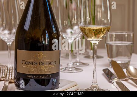 Eine Flasche Conde de Haro Brut Vintage 2012 Cava von Bodegas Muga steht neben einem Glas Schaumwein auf einem gedeckten Tisch im Hotel und Restaurant Kronenschlösschen in Hattenheim, Eltville am Rhein, Hessen, Deutschland. Leere Weingläser und ein Wasserglas stehen dahinter. Der Cava wird nach der traditionellen Flaschenfermentation hergestellt. Bodegas Muga hat seinen Sitz in Haro in der Rioja. Der Cava ist der Aperitif beim Mallorca-Lunch des Michelin-Sterne-Kochs Marc Fosh (Restaurant Simply Fosh, Palma de Mallorca) am 26. Februar 2017. Winzer aus Mallorca und dem Rheingau präsentieren ihre Weine bei Stockfoto