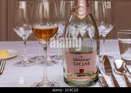 Eine Flasche Schlumberger DOM Rosé Brut, Jahrgang 2013, steht neben einem Glas sprudelndem Rosé auf einem mit einem weißen Tuch bedeckten Tisch beim Galadinner des Michelin-Sterne-Kochs Sebastian Frank im Hotel und Restaurant Kronenschlösschen in Hattenheim, Eltville am Rhein, Hessen, Deutschland. Der Sekt ist der Aperitif des Abends. Das Etikett nennt die "Méthode traditionnelle", die traditionelle Flaschenfermentation. Leere Weingläser stehen hinter der Flasche, und das Besteck liegt rechts. Robert Schlumberger gründete die Schlumberger-Sektkellerei 1842 in Wien. Er war der erste in Aus Stockfoto