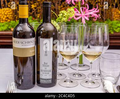 Ein 2012 Furmint von Heidi Schröck und ein 2008 Sauvignon Blanc Ried Vogelsang von Ernst Triebaumer stehen auf einem gedeckten Tisch beim „Österreich Dinner“ (Österreich-Dinner) im Hotel und Restaurant Kronenschlösschen in Hattenheim, Eltville am Rhein, Hessen, Deutschland. Zwei Gläser Weißwein stehen daneben vor leeren Gläsern, Nerinen und Forsythien. Beide Weinbaustellen befinden sich in Rust im Burgenland. Die Weinkellerei Heidi Schröck in Rust am Neusiedler See ist bekannt für Ruster Ausbruch und Furmint. Beim Österreich-Dinner des 21. Rheingau Gourmet & Wein Festivals kocht der mit einem Michelin-Stern ausgezeichnete Koch Simon Taxacher ein „Kul Stockfoto
