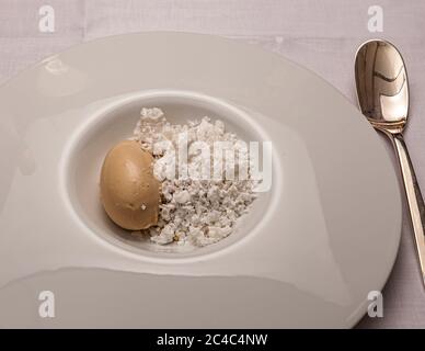 Ein hellbrauner Knödel liegt neben weißen Brötchen in einem tiefen weißen Teller mit breitem Rand, daneben liegt ein silberner Löffel. Dieses Gourmet-Dessert wird am Nachmittag des 11. März 2017 auf dem 21. Rheingau Gourmet & Wein Festival im Hotel und Restaurant Kronenschlösschen in Hattenheim, Eltville am Rhein, Hessen, Deutschland, serviert. An diesem Nachmittag stehen im Veranstaltungsort zwei Mittagskarten zur Auswahl: das ‚Thai–Französische‘ Mittagessen des mit einem Michelin-Stern ausgezeichneten Kochs Henrik Yde Andersen aus dem Restaurant Kiin Kiin in Kopenhagen, Dänemark, und das ‚Kalifornische Raritäten‘-Mittagessen mit einer viergängigen Speisekarte des Gastgebers Koch Simon Stockfoto