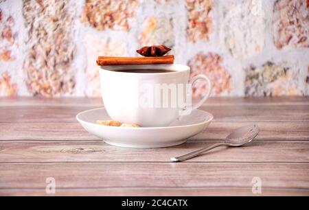 Eine Tasse schwarzen Kaffee auf einer Untertasse mit Zimt, Anis und Rohrzuckerscheiben. Nahaufnahme. Stockfoto