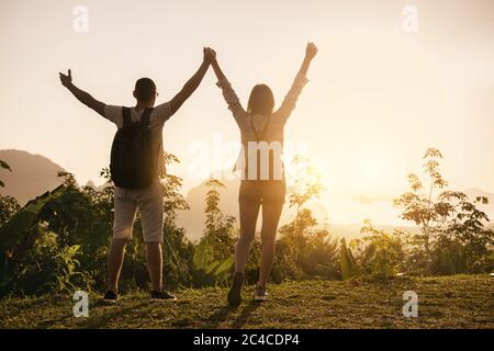 Zwei glückliche Touristen stehen mit erhobenem Arm am Aussichtspunkt und genießen den Sonnenaufgang Stockfoto