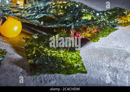 Knusprige Nori-Algen mit Kirschtomaten und dunklen Gewürzen auf grauem Beton. Japanisches Essen Nori. Getrocknete Blätter von Algen. Speicherplatz kopieren. Stockfoto