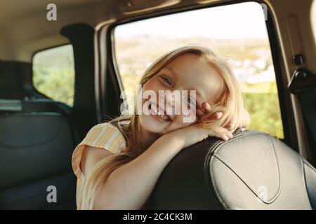 Liebenswert Mädchen sitzt auf dem Rücksitz des Autos. Nettes Mädchen genießen Reisen von einem Auto Blick auf Kamera und lächelnd. Stockfoto