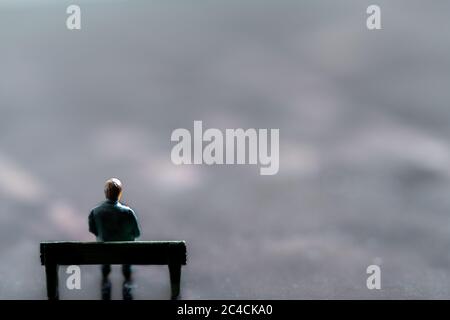 Miniatur-Figur posiert als Mann allein auf einer Bank sitzen in surrealen Landschaft, minimalistisch abstraktes Konzept Bild Stockfoto