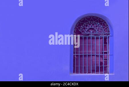 Schmiedeeisernes Fenster auf königlich blauer Betonwand mit Kopierraum Stockfoto