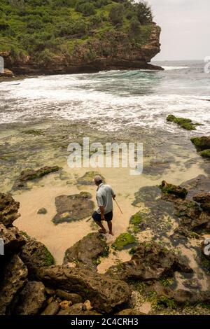 Ein einsame indonesische Fischer geht an einer felsigen Küste entlang. Stockfoto