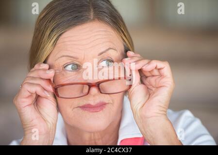 Potrait smart attraktive reife Geschäftsfrau mit Brille und neugierig beobachten Ausdruck, verschwommen Hintergrund. Stockfoto