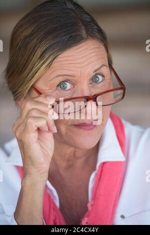 Potrait smart attraktive reife Geschäftsfrau mit Brille und neugierigen Ausdruck, verschwommener Hintergrund. Stockfoto