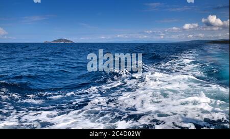 Landschaft mit dem Meer, Insel und schönen Wolken am blauen Himmel. Blaue Meerwasseroberfläche in Bewegung mit Schaum Stockfoto