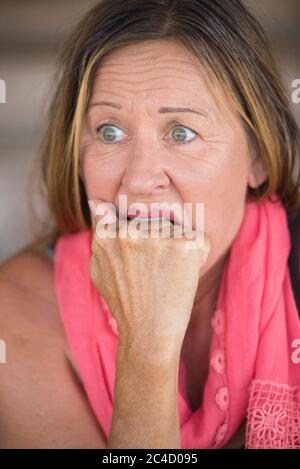 Portrait erschrocken reife Frau, ängstlich, schockiert gestresst, besorgt Gesichtsausdruck, Nagel beißen, Hand zwischen den Zähnen, verschwommener Hintergrund. Stockfoto