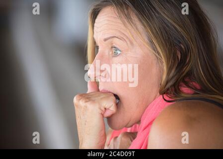 Portrait erschrocken reife Frau, ängstlich, schockiert gestresst, besorgt Gesichtsausdruck, Nagel beißen, Hand zwischen den Zähnen, verschwommener Hintergrund, Kopierraum. Stockfoto
