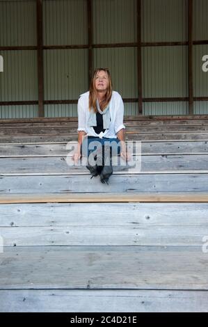 Portrait Attraktive reife Frau sitzt einsam und nachdenklich auf Holztreppe oder Tribüne im Freien, in hohen Fersen Stiletto Stiefel, kopieren Raum. Stockfoto