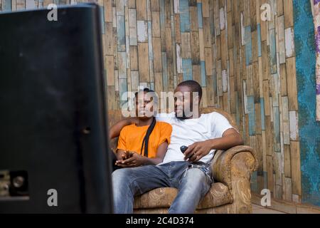 Glückliches afroamerikanisches Paar, das beim Fernsehen sitzt und spricht Stockfoto