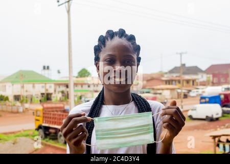 Afroamerikanische Frau, die eine hygienische Gesichtsmaske gegen sie hält Teilfläche während der Isolierung Stockfoto