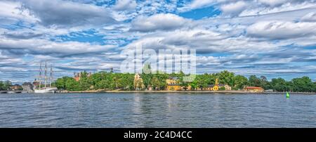 STOCKHOLM SCHWEDEN - 2. AUGUST 2019: Panoramablick auf die Küste der Insel Skeppsholmen mit Booten und Schiffen und bewölktem Himmel Stockfoto