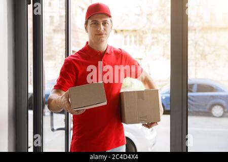 Freundlicher Kurier hält dem Kunden das Paket durch die Schwelle des Hauses aus Stockfoto