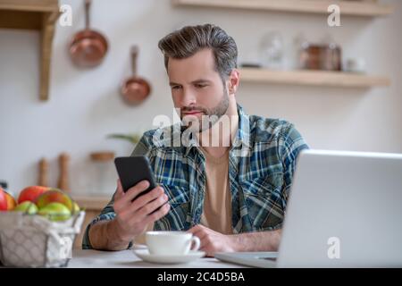 Mann in einem karierten Hemd mit einem Smartphone und einer Nachricht lesen Stockfoto