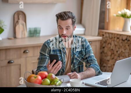 Mann in einem karierten Hemd, der eine Nachricht liest und erstaunt aussschaut Stockfoto