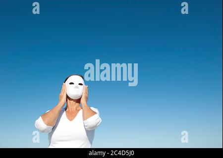 Geheimnisvolle Frau versteckt sich hinter weißen Gesichtsmask, isoliert mit blauen Himmel als Hintergrund und Kopierer Raum. Stockfoto