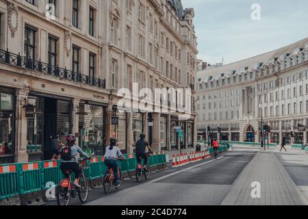 London, Großbritannien - 13. Juni 2020: Gruppe von Radfahrern, die an geschlossenen Geschäften auf einer leeren Regent Street, einer großen Einkaufsstraße im West End von London, vorbeifahren. Stockfoto