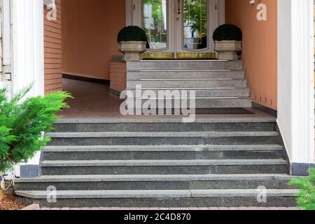 Marmorstufen steigen bis zur Schwelle des Hoteleingangs mit steinernen Blumentöpfen mit grünen Büschen, aus nächster Nähe. Stockfoto