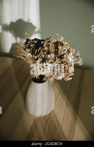 Schöner Blumenstrauß in rosa Keramik Vase auf Holztisch im Nachmittagslicht mit weißer Wand im Hintergrund Stockfoto