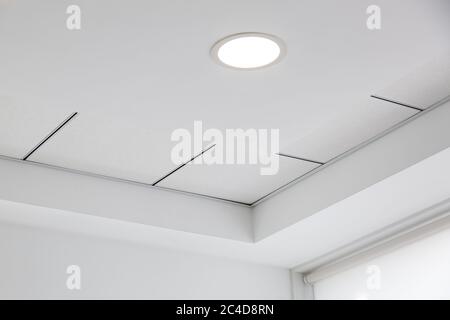 Mehrstufige Decke mit dreidimensionalen Aussprüngen und einer abgehängten Fliesendecke mit eingebautem runden LED-Licht. Stockfoto