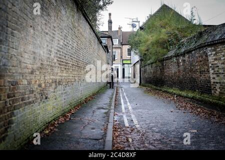 Atmosphärisches Bild eines älteren Mannes, der im frühen Winter alleine eine dunkle Einbahnstraße in die britische Straße hinunterging. Stockfoto