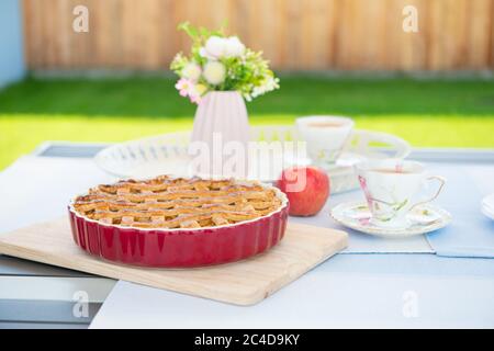 Frisch gebackene Apfelkuchen, Tasse Tee und Blumen auf einem Tisch zu Hause auf der gemütlichen Terrasse Stockfoto