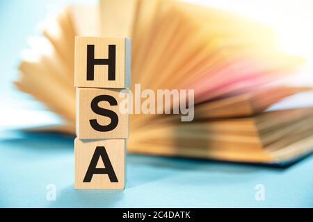 Holzwürfel mit der Abkürzung HSA Health Sparkonto auf dem Hintergrund eines offenen Buches. Stockfoto