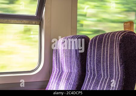 Paar leere Bahnkutschensitze auf einer Pendlerfahrt. Der Zug fährt mit Geschwindigkeit, wie man von der Unschärfe des nahegelegenen Grüns sieht. Stockfoto