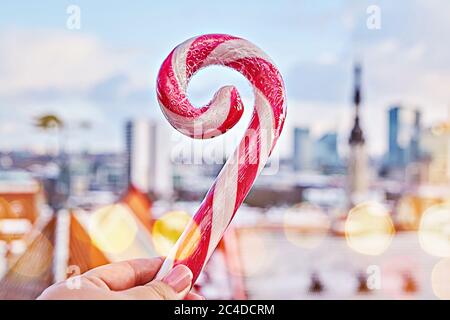 Nahaufnahme des gestreiften Zuckerrohrs Lollipop in der Hand gegen die Altstadt von Tallinn. Ikonischer Blick auf die Skyline von Tallinn von der Aussichtsplattform Stockfoto
