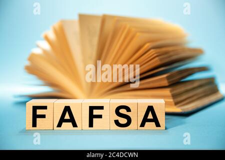 Holzwürfel mit der Abkürzung Free Application for Federal Student Aid FAFSA auf dem Hintergrund eines offenen Buches. Stockfoto