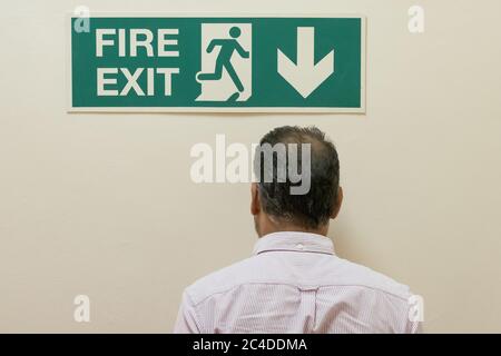Mann sah, wie er in eine feste Wand ging, unter einem Schild mit dem Feuerausgang in einem Bürokomplex. Der eigentliche Feuerausgang ist die Treppe hinunter.