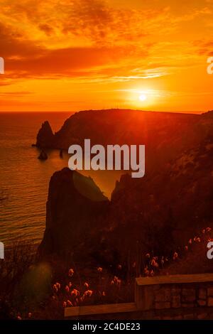 Ein rot brennender Sonnenuntergang mit dem Silhouett einer Klippe über dem Meer Stockfoto