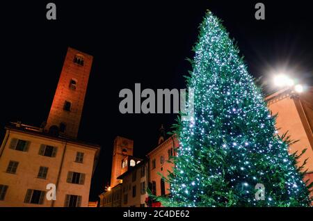 Piazza Risorgimento, Hauptplatz von Alba (Piemont, Italien) bei Nacht mit dem Rathaus, den mittelalterlichen Türmen und einem beleuchteten weihnachtsbaum Stockfoto