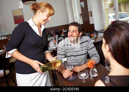 Kellnerin im Restaurant gießt Weißwein in ein Glas Stockfoto