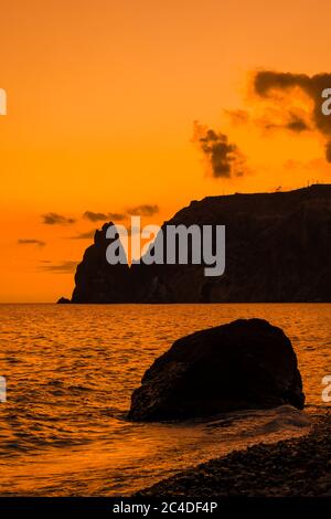 Ein rot brennender Sonnenuntergang mit dem Silhouett einer Klippe über dem Meer Stockfoto