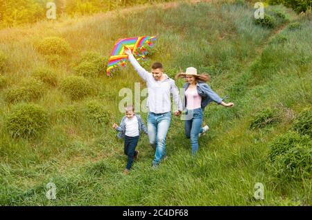 Sommer Aktivitäten für die Familie. Fröhliche junge Eltern mit ihrem Sohn fliegen Drachen zusammen in der Landschaft Stockfoto