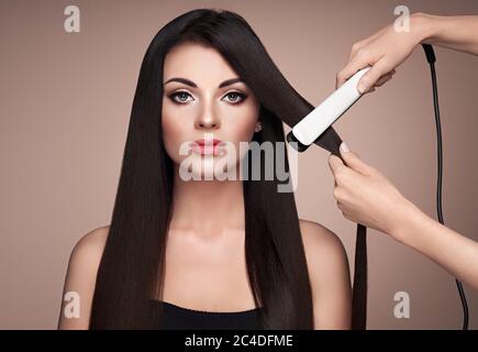 Friseur glätten lange dunkle Haare mit Fön Bügeleisen. Schöne Frau mit langen, glatten Haaren. Glatte Frisur Stockfoto