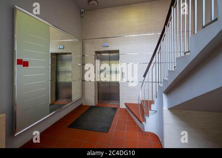 Moderne Eingangshalle im Wohnkomplex. Großer Spiegel, Aufzug und Treppen. Teppich auf roten Fliesen. Stockfoto